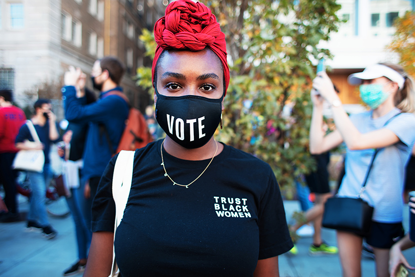 A black woman wearing a mask that says VOTE.