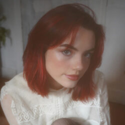 Red-haired Genevieve Stokes looking up at the camera in a white blouse.