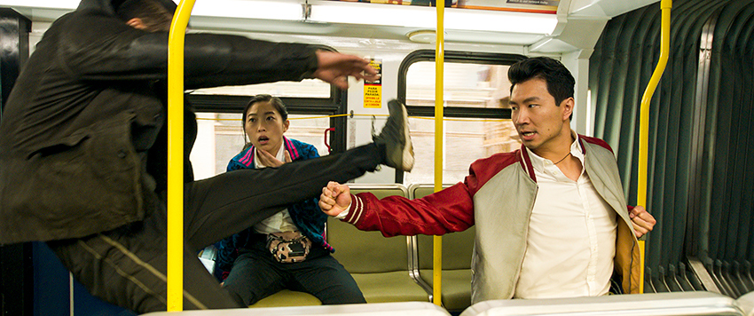 Simu Liu fighting a man inside a bus with Awkwafina in the background.
