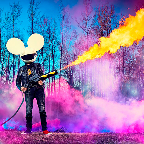deadmau5 standing in blue and pink lit outdoor setting with a blowtorch.