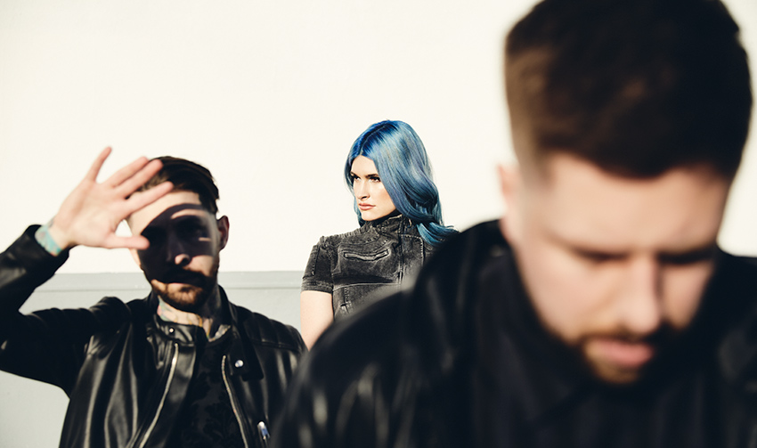 Michael Stringer, out of focus in the foreground, Bill Crook behind him blocking the sun from his face with his hand, and Courtney LaPlante centred in the background with her blue hair.