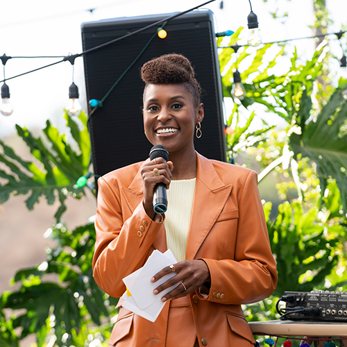Issa Rae in an orange suit holding a mic, from TV show Insecure