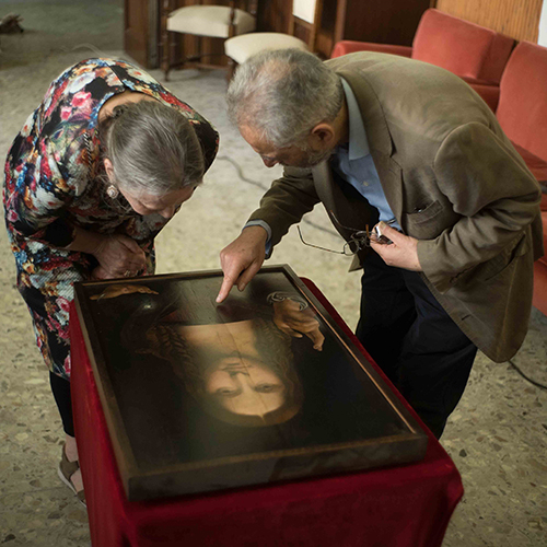 Two people looking down at a painting atop a table draped in red fabric.