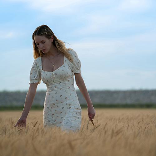 Dylan Penn walking in a wheat field in a white dress.
