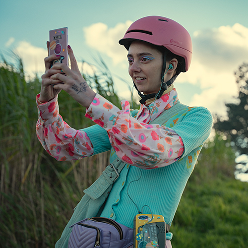 A girl wearing a pink helmet taking a photo on her phone.