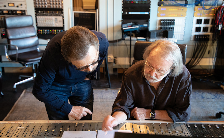 Björn Ulvaeus and Benny Andersson of ABBA leaning over the sound mixing board in their recording studio.