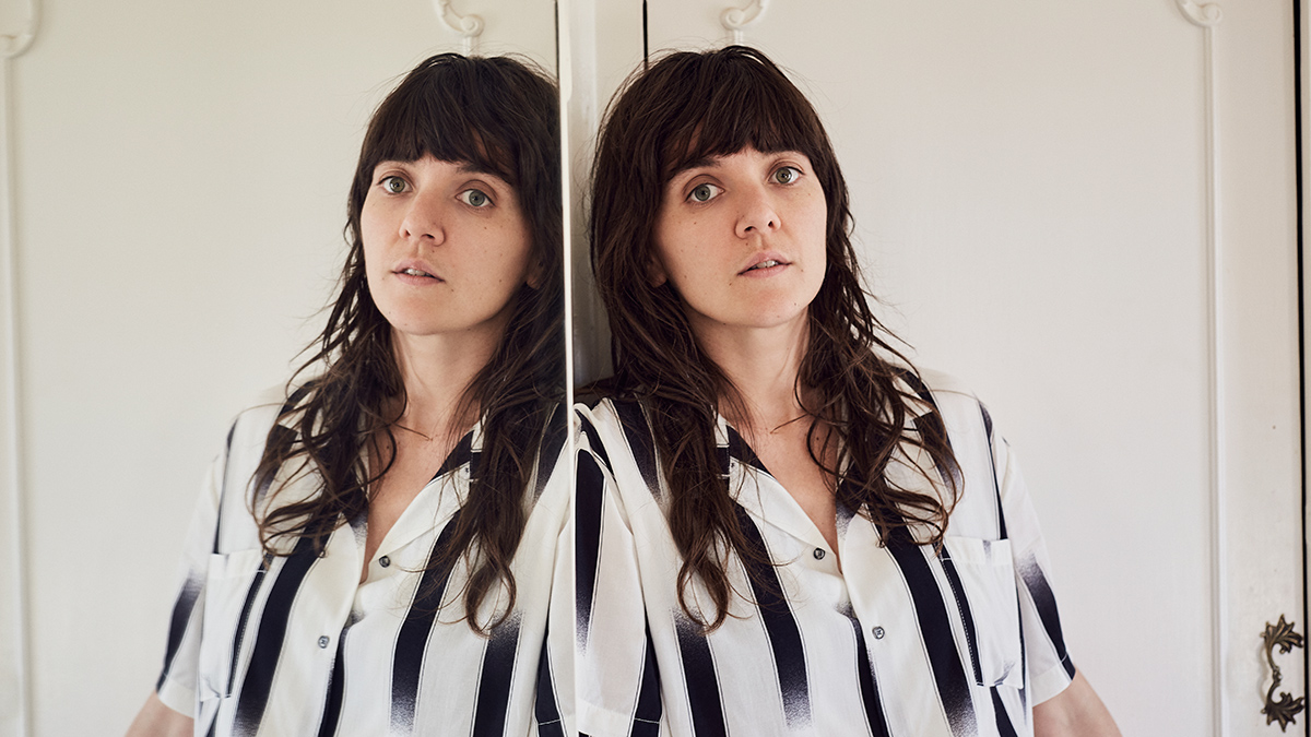 Courtney Barnett leaning against a full length mirror in a black and white top.
