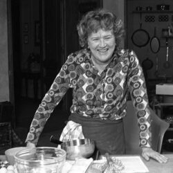 A black and white photo of Julia Child standing at her kitchen counter.