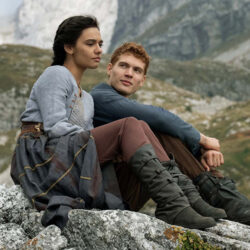 Scene from Wheel of Time of a woman and a man sitting on a bouldered hill.