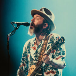 Dallas Green performing on stage a Hawaiian-style button-down in pine tree print and a felt Panama hat.